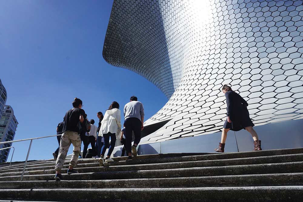 A group of people walking up stairs in front a sweeping, hexagon clad structure.