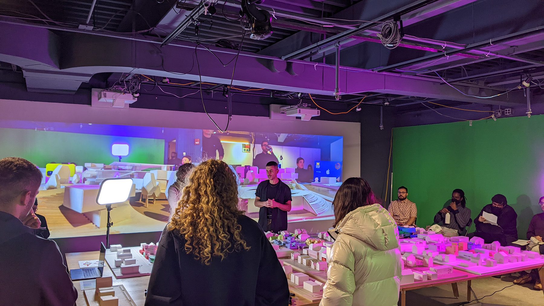 A class gathers around a large model city lit by neon lights in the TVLab