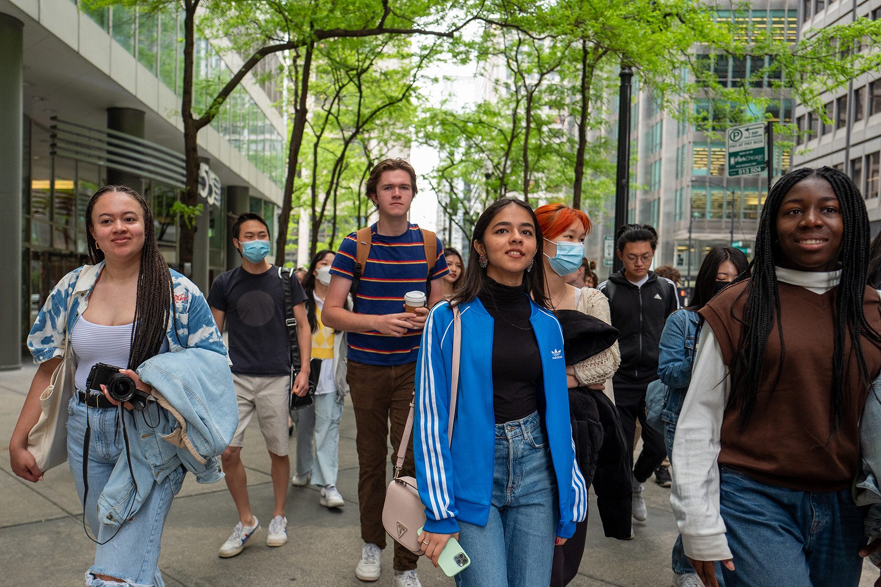 A group of students walks through a downtown corridor of buildings and greenery.