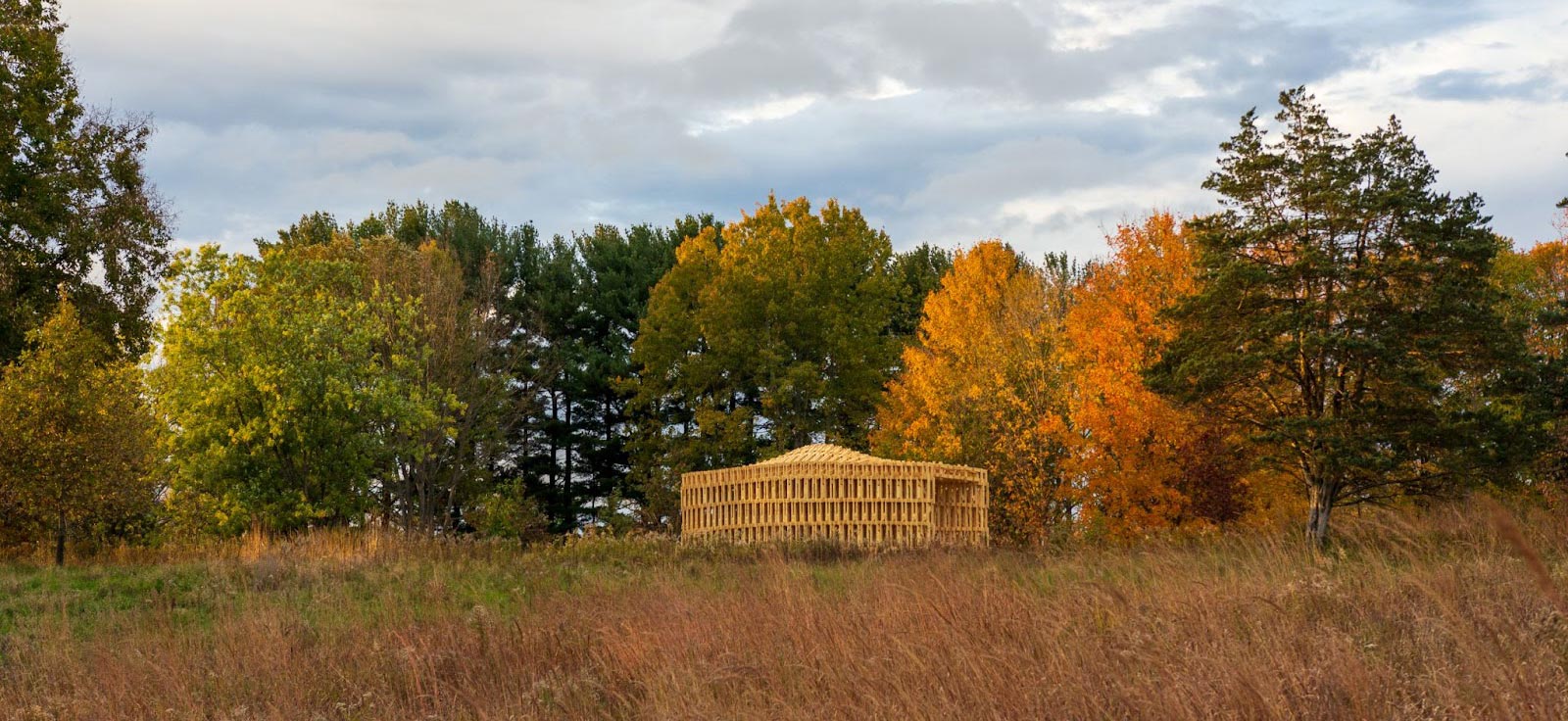 Robotically Fabricated Structure (RFS) amongst a grass field and trees with colorful fall foliage
