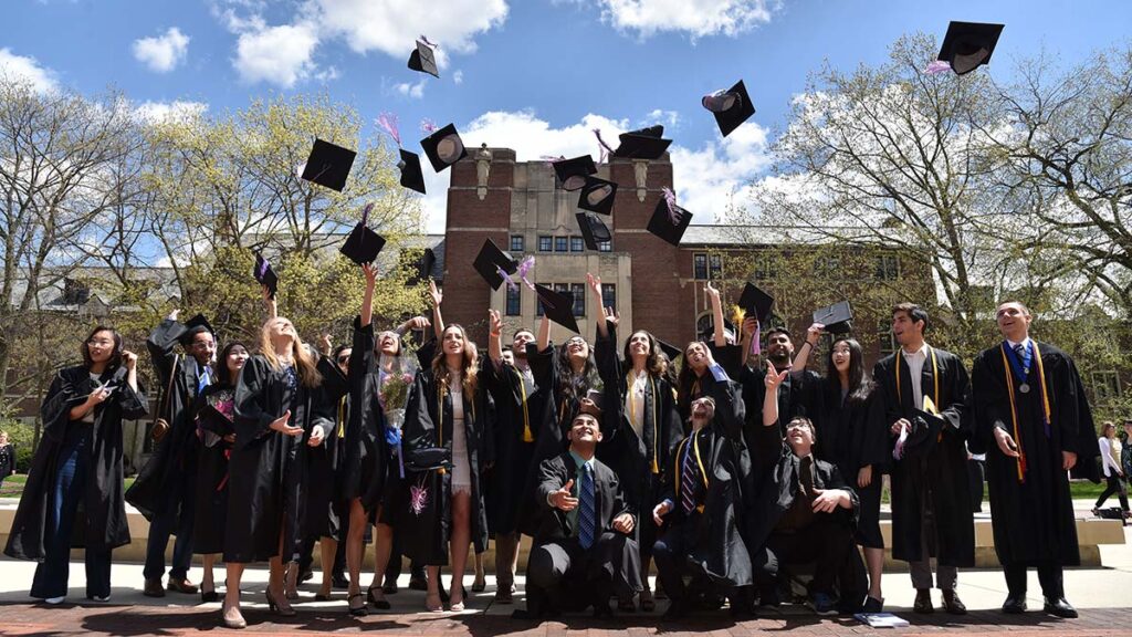 A group of students wearing commencement caps and gowns throwing their caps into the air.
