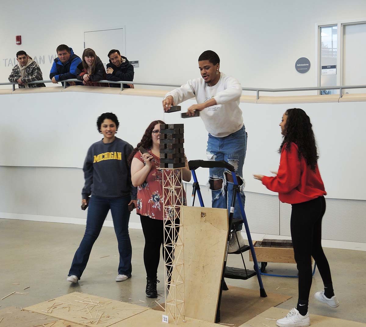 A group of students placing weights on a wooden tower structure to test it's load bearing capacity.