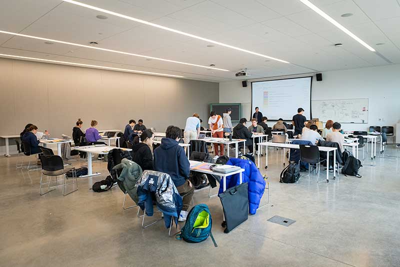 Students working at tables in a large classroom