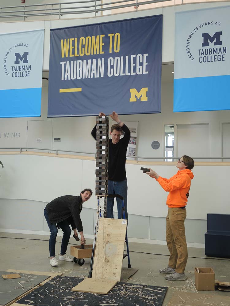 Students adding weights to the top of a wooden tower structure to test the strength of the tower.