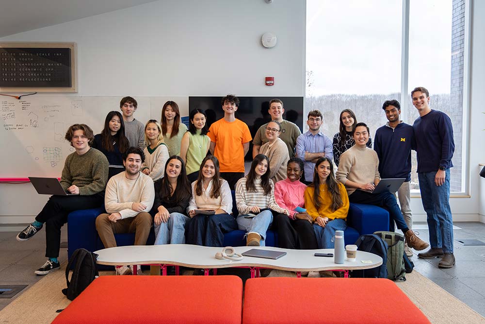 A group of people sitting on and standing around a couch looking at the camera.