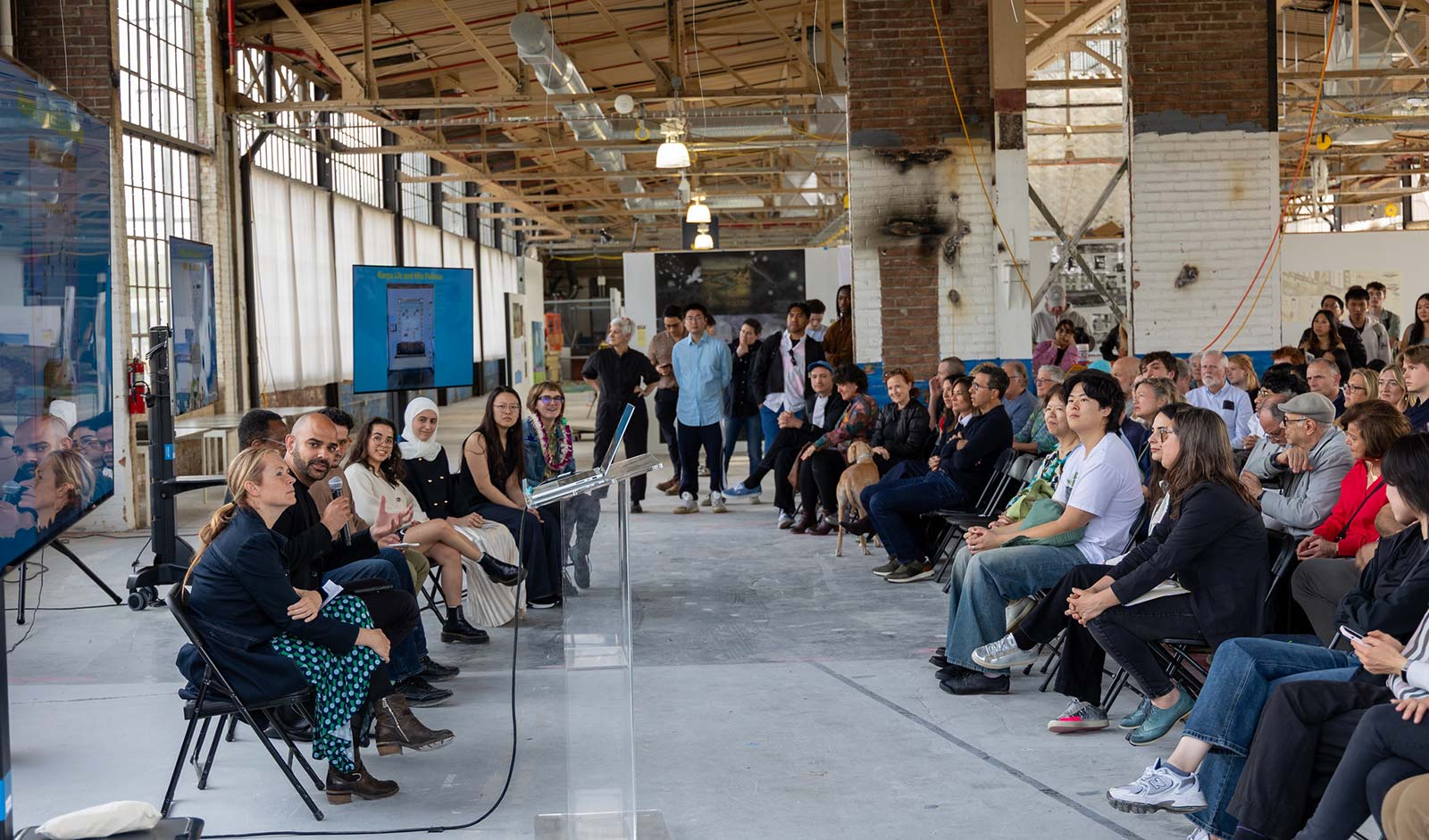 A group of people watching a panel of jurists award and comment on student work.