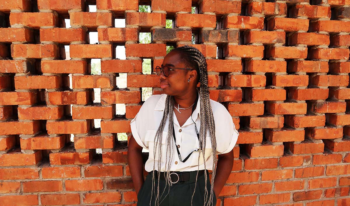 Portrait of Kuukuwa Manful standing against a brick background