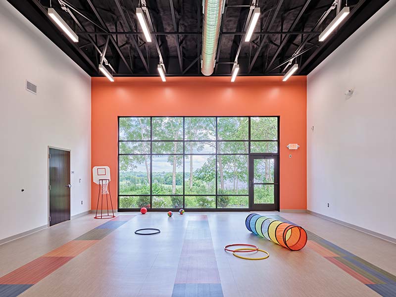 A bright room with large windows, colorful floor patterns, and children’s play equipment.