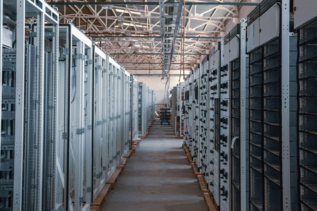 Long rows of tall server racks line a large industrial room, forming a central aisle.