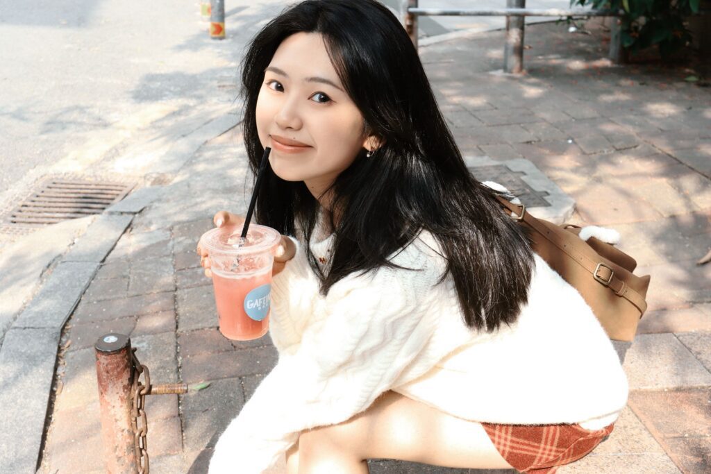 A portrait of Shiyu Xiong crouching down with a drink in hand