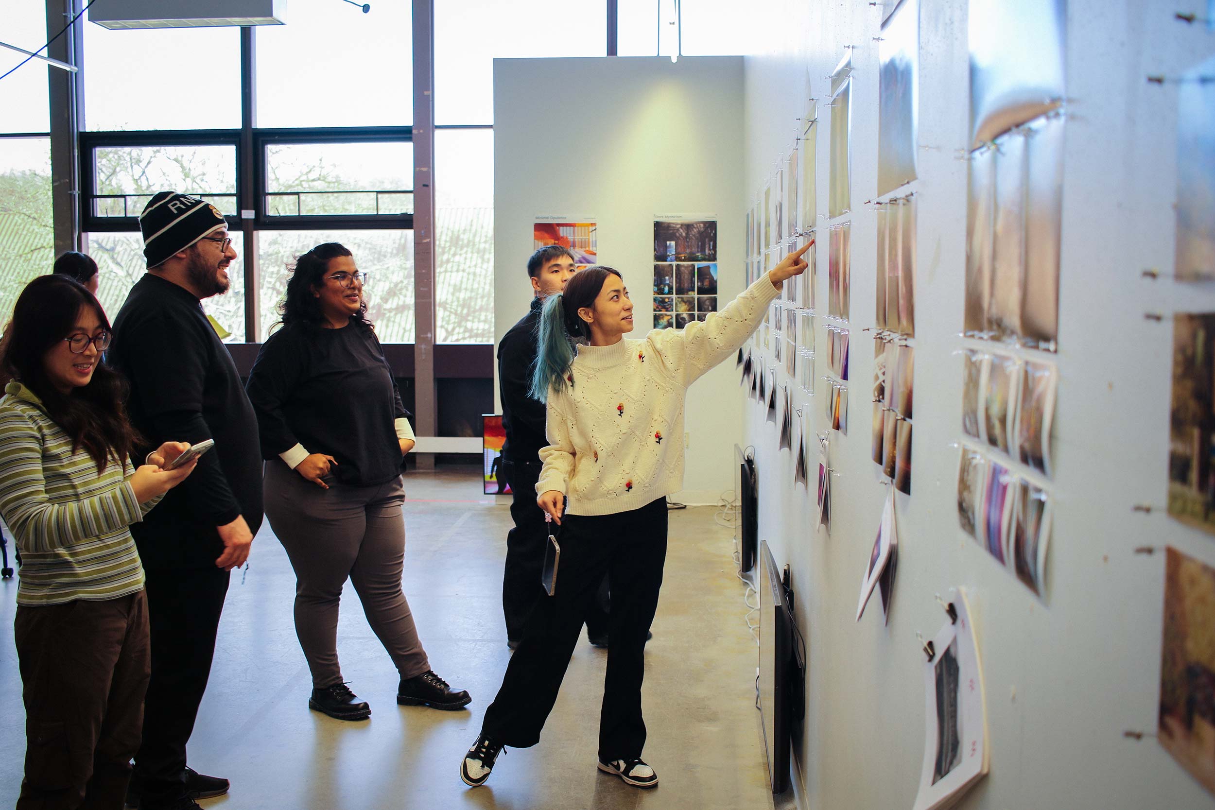 A small group of people stands in a studio space while one person points to photographs displayed on a wall.