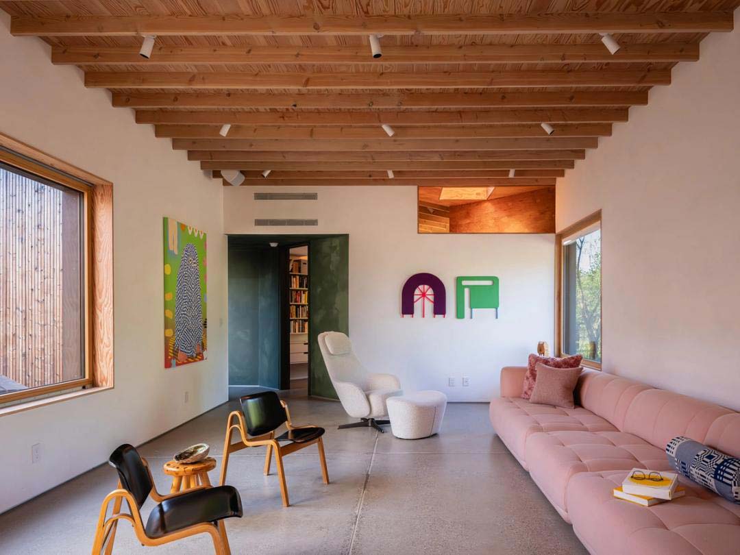 Bright living room with exposed wood ceiling beams, pink sofa, modern chairs, and colorful wall art.
