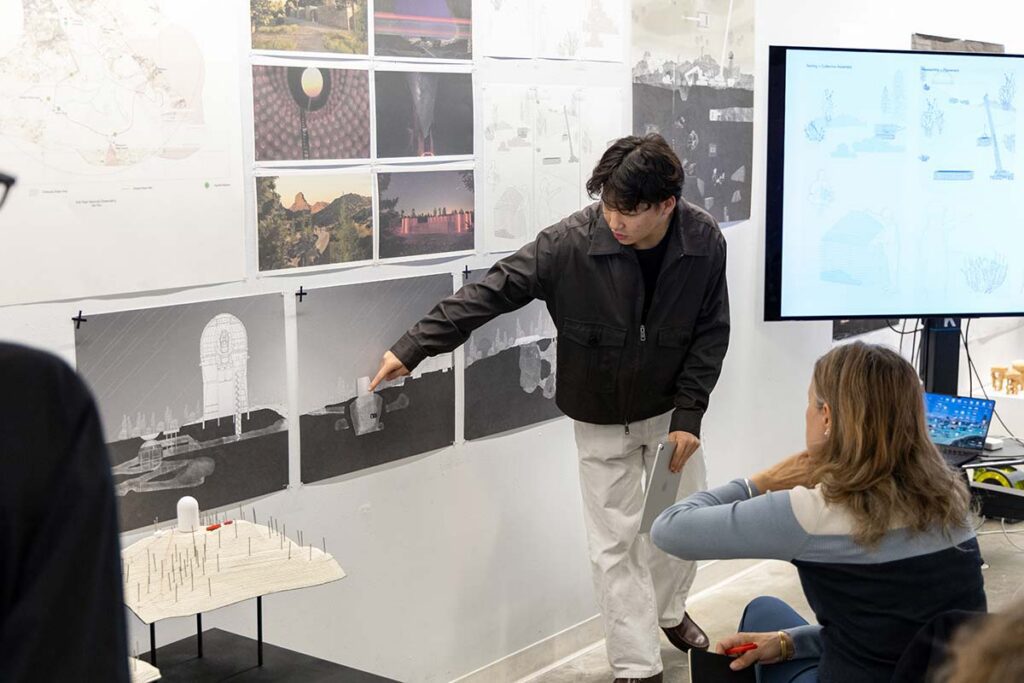 Student presenting work that is pinned up on the wall