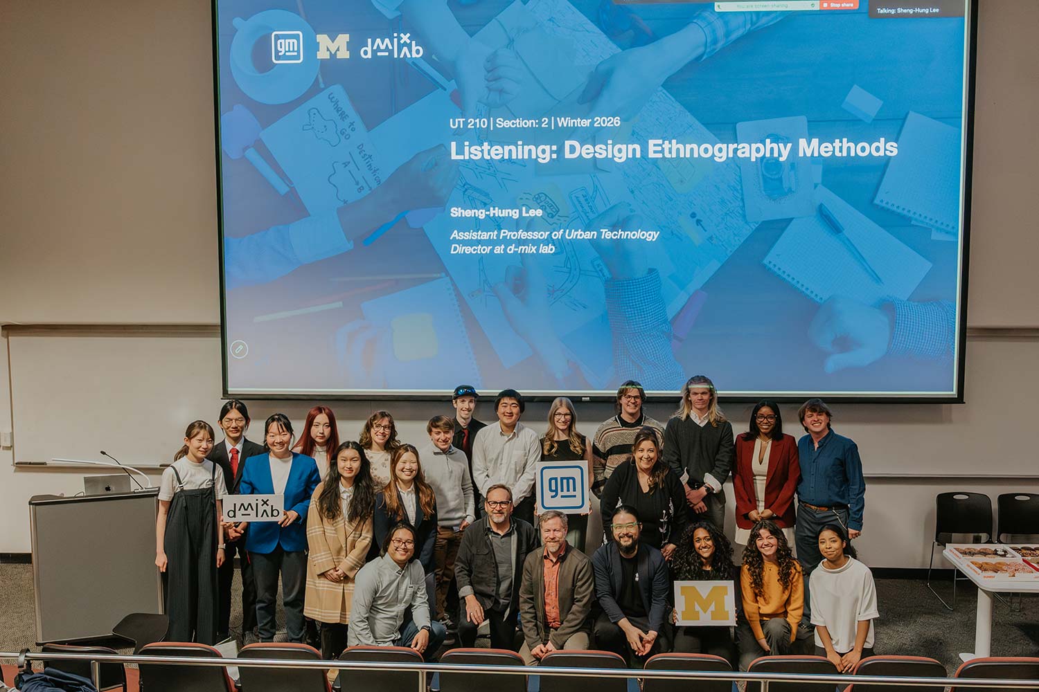 Group poses in a lecture hall below a slide titled “Listening: Design Ethnography Methods.”