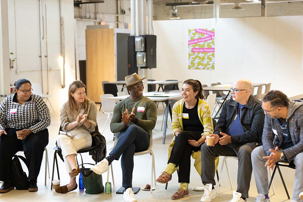 A group of people sitting in chairs and smiling while listening to a presentation