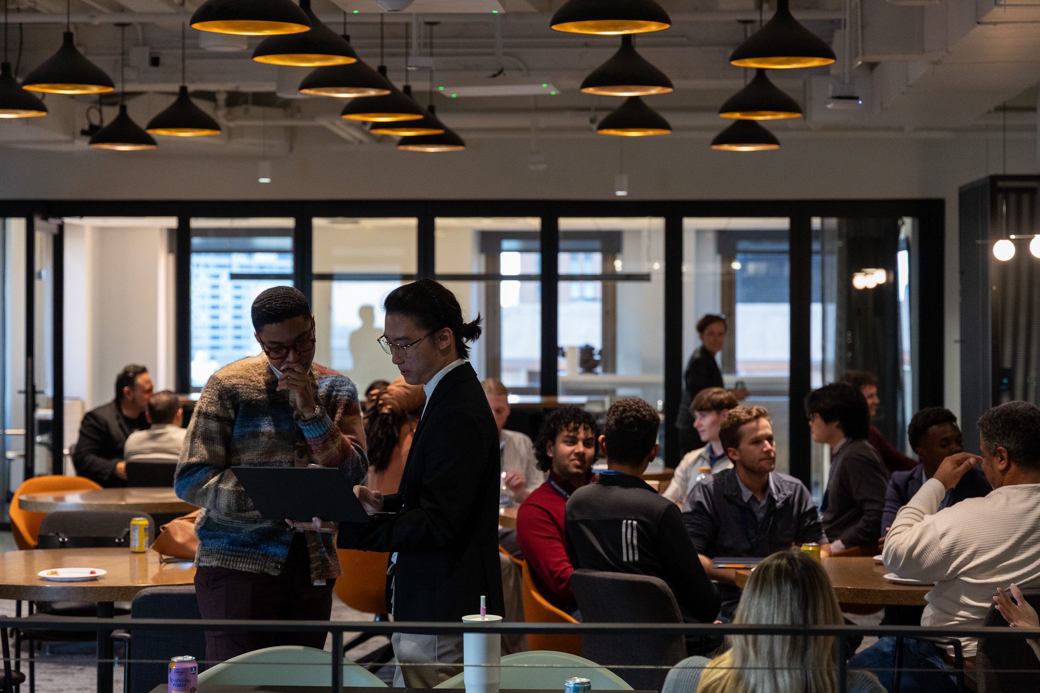 A student and an alumni look at a computer in front of a crowd of sitting students