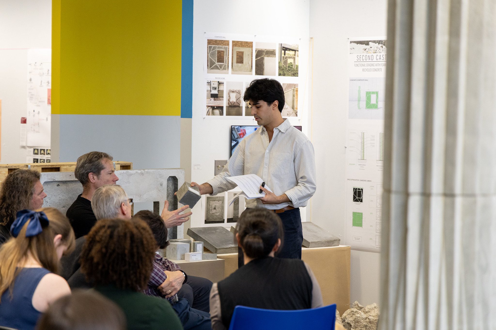 A student hands a piece of cement to a faculty member during final reviews